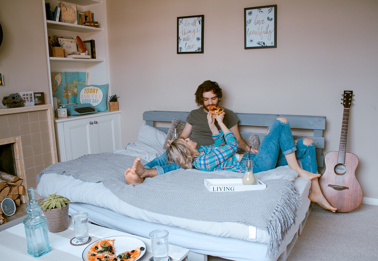 A couple enjoying pizza together while sitting on a bed, sharing a casual and cozy moment.