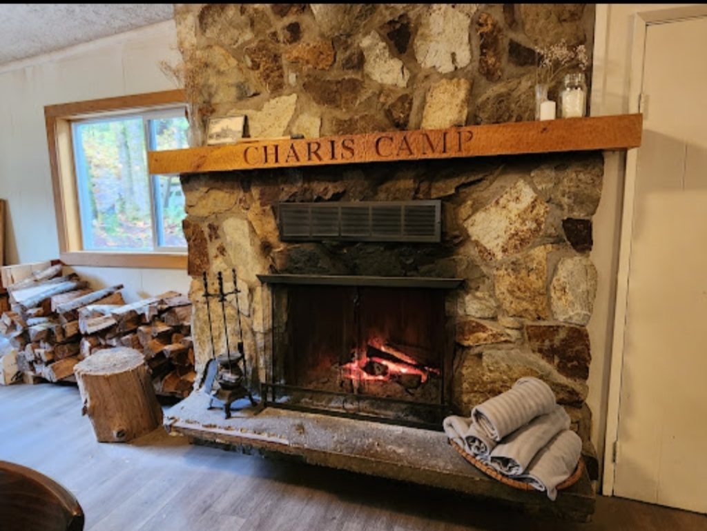 A rustic fireplace with a decorative sign stating "Charis Camp," contributing to a homely and inviting setting.